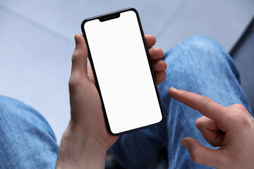 Man holding smartphone with blank screen indoors, closeup. Mockup for design