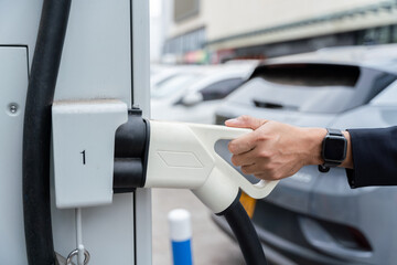 Hand of A man holding Electric Car Charging connect to Electric car on electric car charging station. Concept of green energy and reduce CO2 emission. EV car.