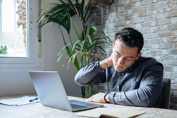 Exhausted young Caucasian male worker sit at desk massage neck suffer from strain spasm muscles....