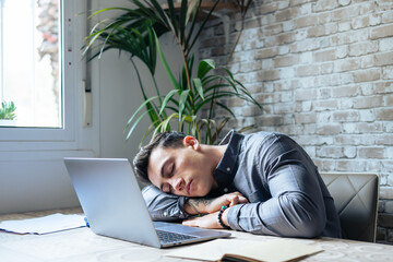Exhausted young Caucasian male employee sleep desk at office overwork preparing report. Tired male fall asleep doze off at workplace, work late to meet deadline. Fatigue, exhaustion concept.. - obrazy, fototapety, plakaty
