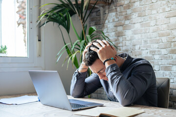 Unhappy young Caucasian male worker in glasses look at laptop screen shocked by gadget breakdown or...