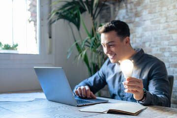 Crop close up of male employee work on computer hold bright light bulb get brilliant business idea. Businessman or worker feel motivated with successful startup project in office. Innovation concept..