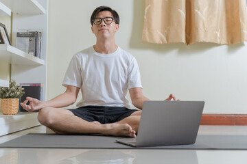 Healthy Asian young business man using laptop for learning online yoga for meditation. Businessman...