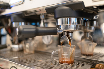 Close up of Espresso coffee pouring from machine. Barista tamp ground coffee, use machine for espresso pouring coffee to making coffee at coffeeshop or cafe.