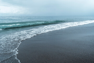 Black volcanic sand on the beach with waves. © SOLDATOOFF