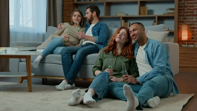 Two ethnic couple diverse men women watch television romantic tv film at home family rest on sofa and floor multiracial friends watching comedy movie comfortable leisure in apartment with bottled beer