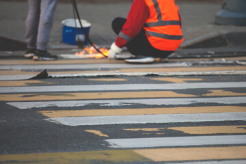 Process of making new road surface markings with a line striping machine, workers improve city infrastructure, demarcation marking of pedestrian crossing with hot melted paint on asphalt pavement