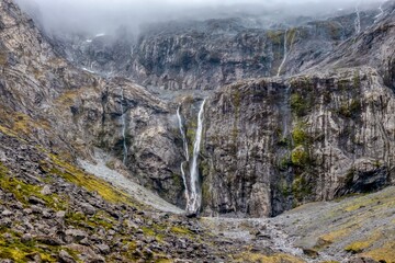 Waterfalls, mist and rain over a steep wall of granite on the South Island of New Zealand, near the entrance to the Homer Tunnel which leads to Milford Sound.