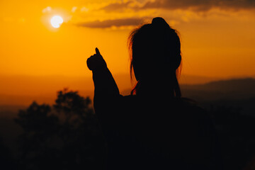 silhouette young woman is pointing at the sunset.