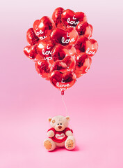 Love composition made of teddy bear and Bunch of red color heart shaped foil balloons on pastel...