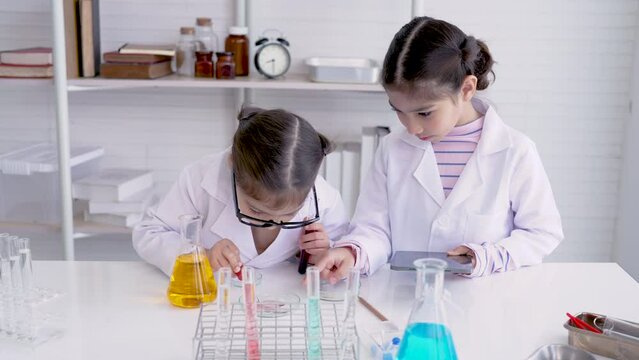 4K, Two kid Asian girls, standing in science room, Mixing paints, doing chemistry experiments, used squeeze tube squeeze out colored water drop into test cup, Another person holds laptop take notes.