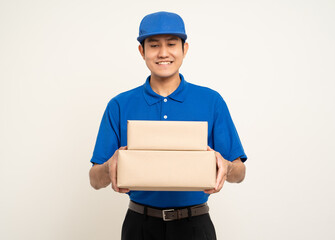 Happy delivery asian man in blue uniform standing holding box parcel cardboard on isolated white background. Smiling male service worker. Delivery courier and shipping service.