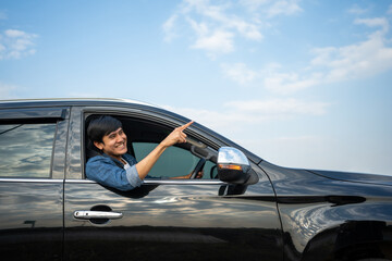 A young Asian man drives a car on a clear day. With beautiful blue sky. He smiling driving to travel by car. Sticking her head outta the windshield