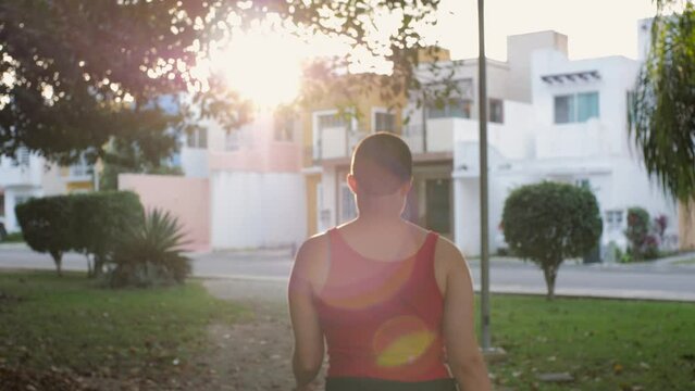Shaved Head Young Latina Lesbian Woman Walking in the Park with Confidence and Smiling. LGBT slow motion scene of young non-binary girl walking while covered by a beautiful solar flare in 4K