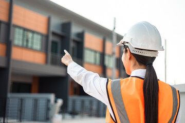 Confident engineer woman standing at modern home building construction. Architect with white safety helmet at construction site. Mechanic service factory Professional work job occupation in uniform.