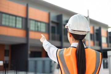 Confident engineer woman standing at modern home building construction. Architect with white safety helmet at construction site. Mechanic service factory Professional work job occupation in uniform.