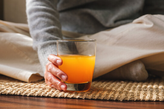 Closeup image of a woman holding and drinking fresh orange juice at home