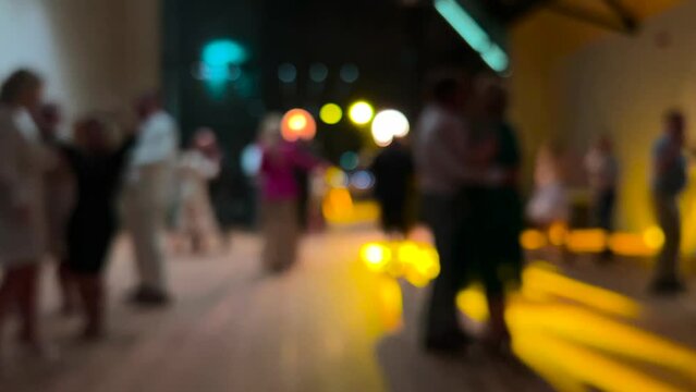 Blurred image of people dancing at a special event. Colorful lights reflect and illuminate the lens