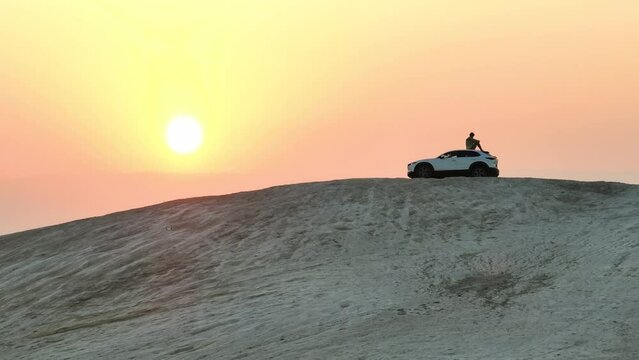 Man sits on a desert hill overlooking a sunrise in ontop of a Mazda car; Israel in the Judean Desert looking out to Jordan.