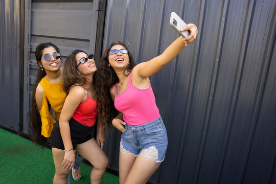 Portrait of beautiful indian women having fun party taking pictures with smart phone,Group of young girl friends in sunglasses and casual clothes laughing and celebrating all together. summer vacation