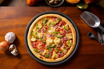 Top view of fresh baked homemade pizza on wooden table with ingredients and spices. Delicious Italian pizza is ready for deliver. Hawaiian Pizza with bell pepper bacon and pineapple.