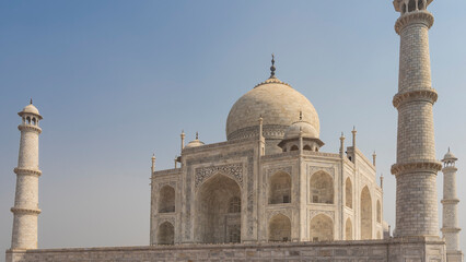Fototapeta na wymiar Beautiful ancient white marble Taj Mahal against the blue sky. The symmetrical mausoleum with arches, domes, minarets is decorated with ornaments, inlays of precious stones. India. Agra.