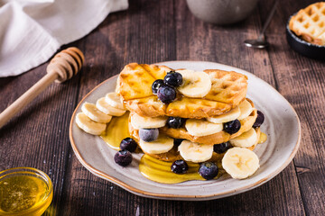 A stack of waffles with banana, blueberries and honey on a plate. Comfort food.