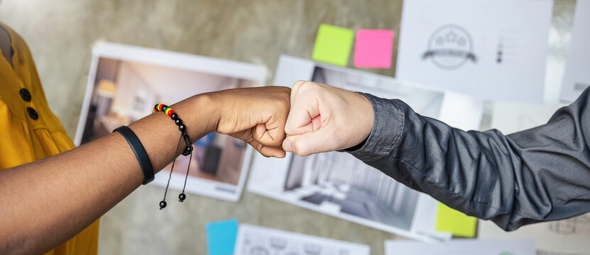 People bumping fists together. Mixed race partners give fist bump, agree to work together, rejoice success and synergy brain storm cooperation in creative artist or graphic interior design background.