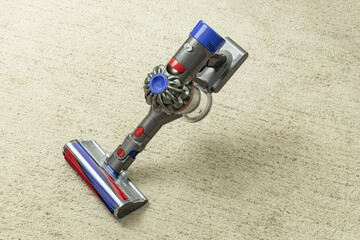 Close-up of a cordless vacuum cleaner on light carpet with copy space. © Serhii