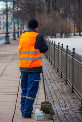 Migrant janitor in bright vest rests while working on the sidewalk.