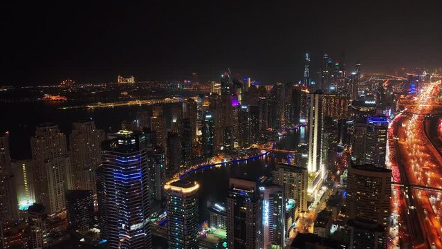 Aerial view of buildings in modern urban borough. Revealing of busy wide multilane highway leading through night city.