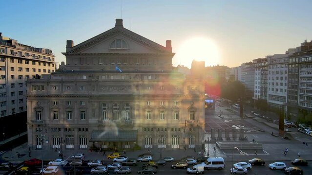 Aerial view drone flying close towards teatro col&oacute;n opera house building with big bright glowing sun in the background at sunset and heavy traffics on 9 de julio avenue at rush hour.
