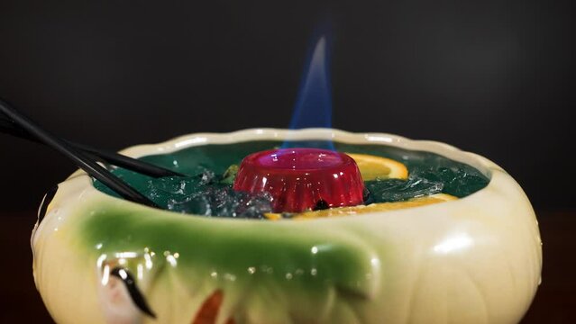 Tropical tiki style cocktail in large bowl with orange slices, burning flame sake punch beverage, slider close up 4K