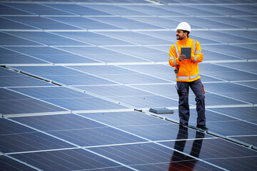 Renewable energy engineer walking through large solar power plant and checking electricity production on his laptop computer. Sustainable energy source and eco friendly technologies.