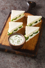 Obraz na płótnie Canvas cucumber sandwich is a crustless tea sandwich composed of thin slices of cucumber situated between two thin slices of lightly buttered white bread closeup on the wooden board on the table. Vertical