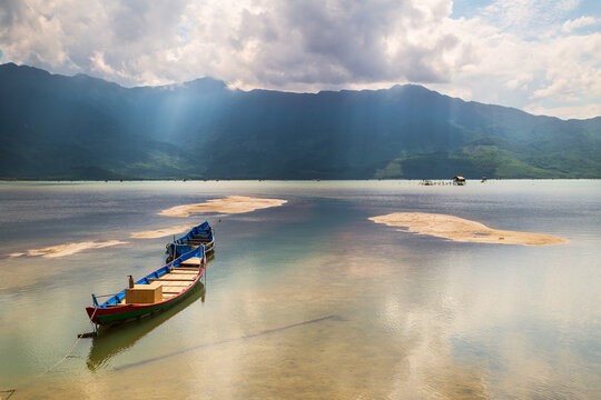 A wooden fishing boat sitting on a calm coastal lagoon in front of a mountain range at Lang Co in Vietnam