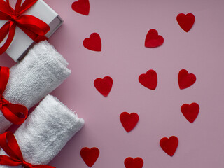 Flat lay with a lot of tiny heart-shaped papers, two towels and gift box. Red heart paper background with towels tied with a red bows. Valentines day spa, bath, self care and body care concept.