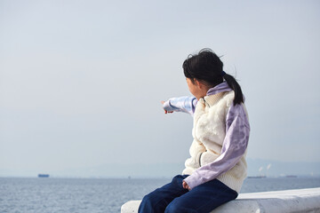 冬の海岸の堤防で遊んでいる小学生の女の子の様子