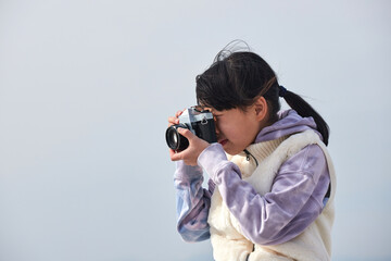 Fototapeta premium 冬の屋外で古いフィルムカメラを遊んでいる小学生の女の子の様子