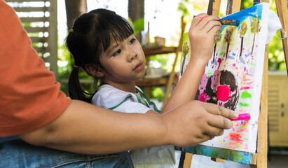 Young Asian Artist girl doing color painting on canvas with art teacher teaching in art school