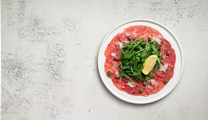 Beef carpaccio with capers, arugula and parmesan on a gray concrete background, view from above, copy space