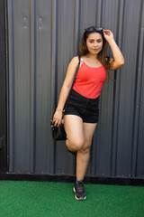 Young attractive fashionable indian woman wearing casual short outfit and handbag standing outdoor. Copy space.