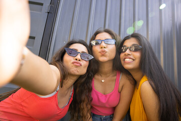 Portrait of three indian friends fun girls wearing sunglasses and colorful outfit taking photos...