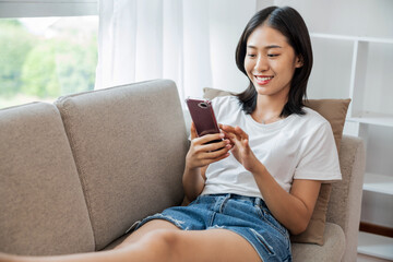 Young asian girl sitting on sofa using mobile phone in the living room.