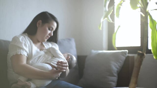 madre hispana sentada arrullando a bebé latino mientras realiza lactancia materna, LME
