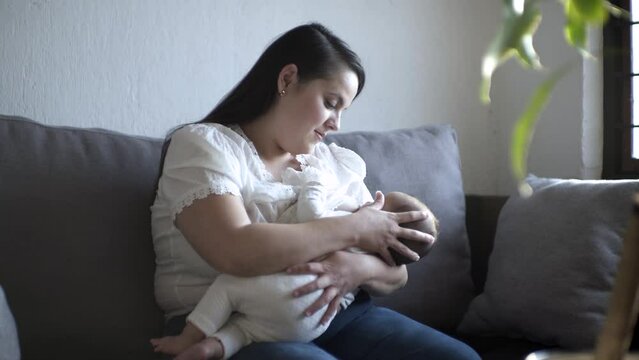 Mamá latina sentada alimentando a su bebe con el pecho realizando lactancia materna y viendo a su hija succionar.
