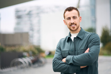 Young attractive tourist looking at camera arms crossed while posing at the urban background, copy...
