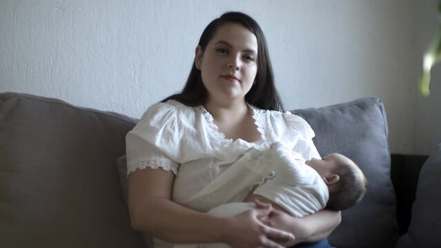 Retrato de madre hispana sentada amamantando a su hijo mientras mira a la cámara.