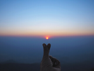 Silhouette Mini hand heart shape over sunrise in the sky background.