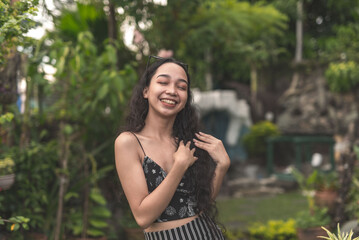 Naklejka premium A pretty young Filipina woman with curly hair wearing a nice black top and long skirt feeling fresh at the garden.